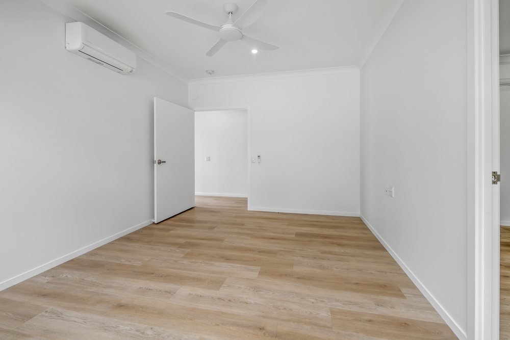A room with a ceiling fan, a split-system air conditioner and a window to the yard.
