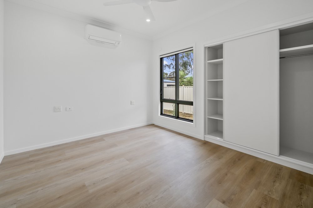A bedroom with built-in shelving, a wardrobe and a window to the yard.