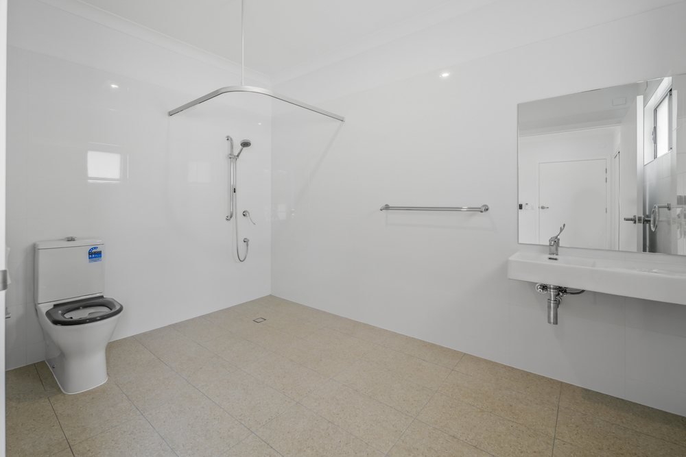 An accessible ensuite with a step-free shower, grab rails and a wall-mounted basin.