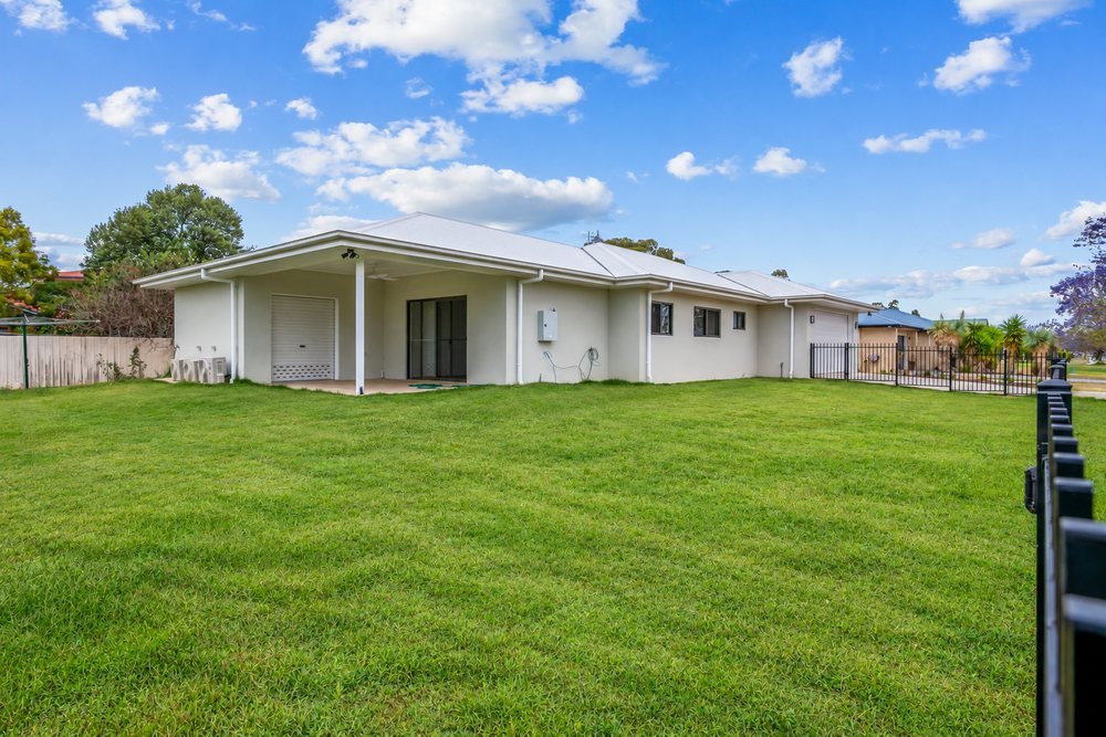 The side of the home, with a large lawn and a black metal fence.