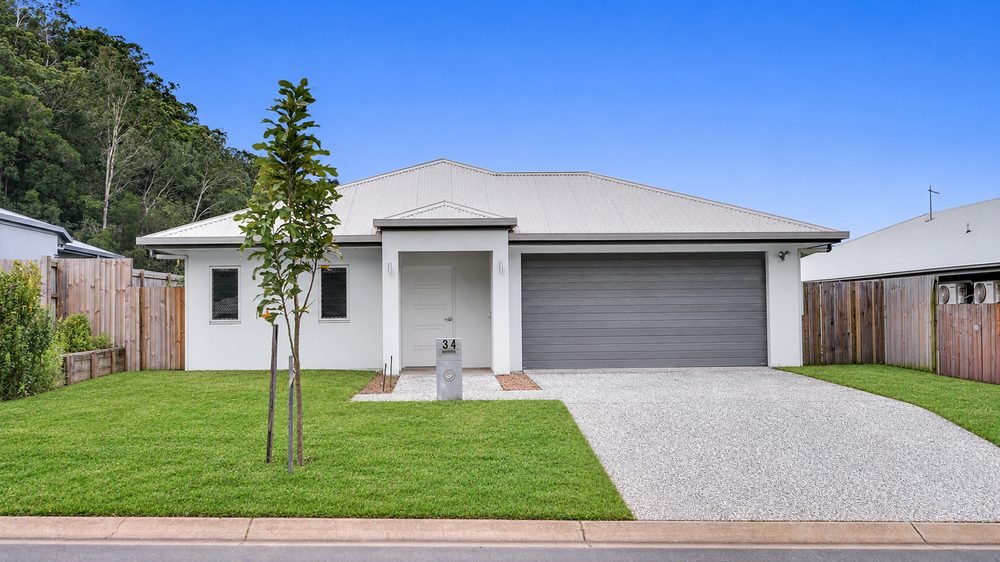 The front of 34 Macaranga Road: a single-storey home with a double garage and a front lawn, with hills behind.