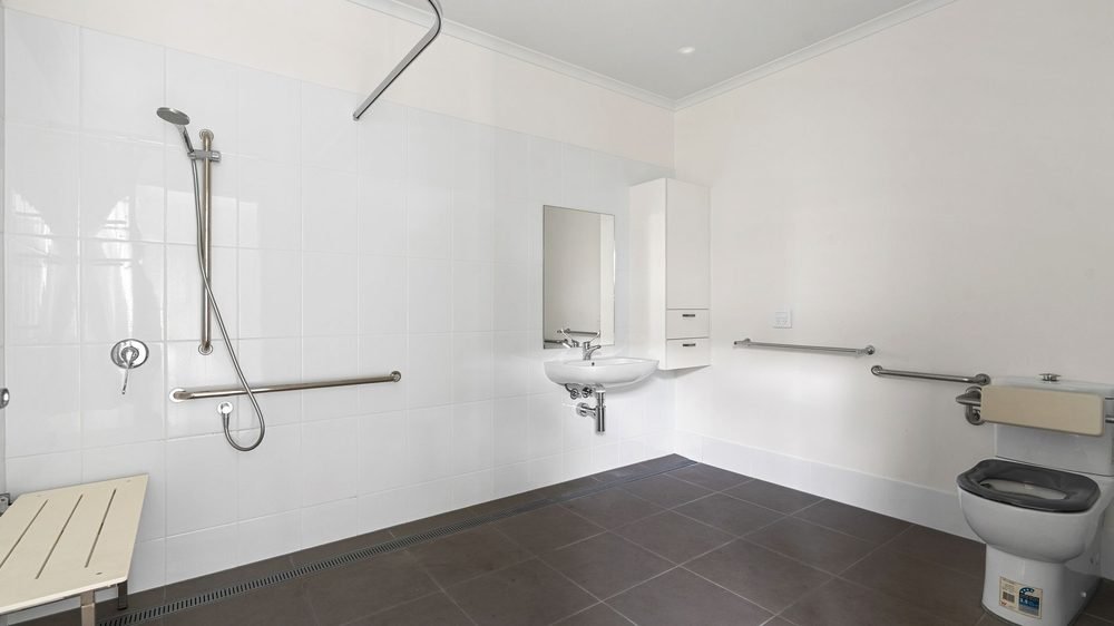 An accessible ensuite with grab rails, a step-free shower and a wall-mounted basin.